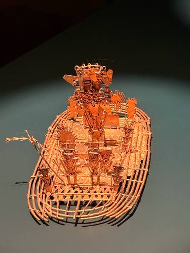 La Balsa Muisca: una balsa de oro con pequeñas figuras de pie sobre una cubierta de varillas, iluminada sobre fondo oscuro